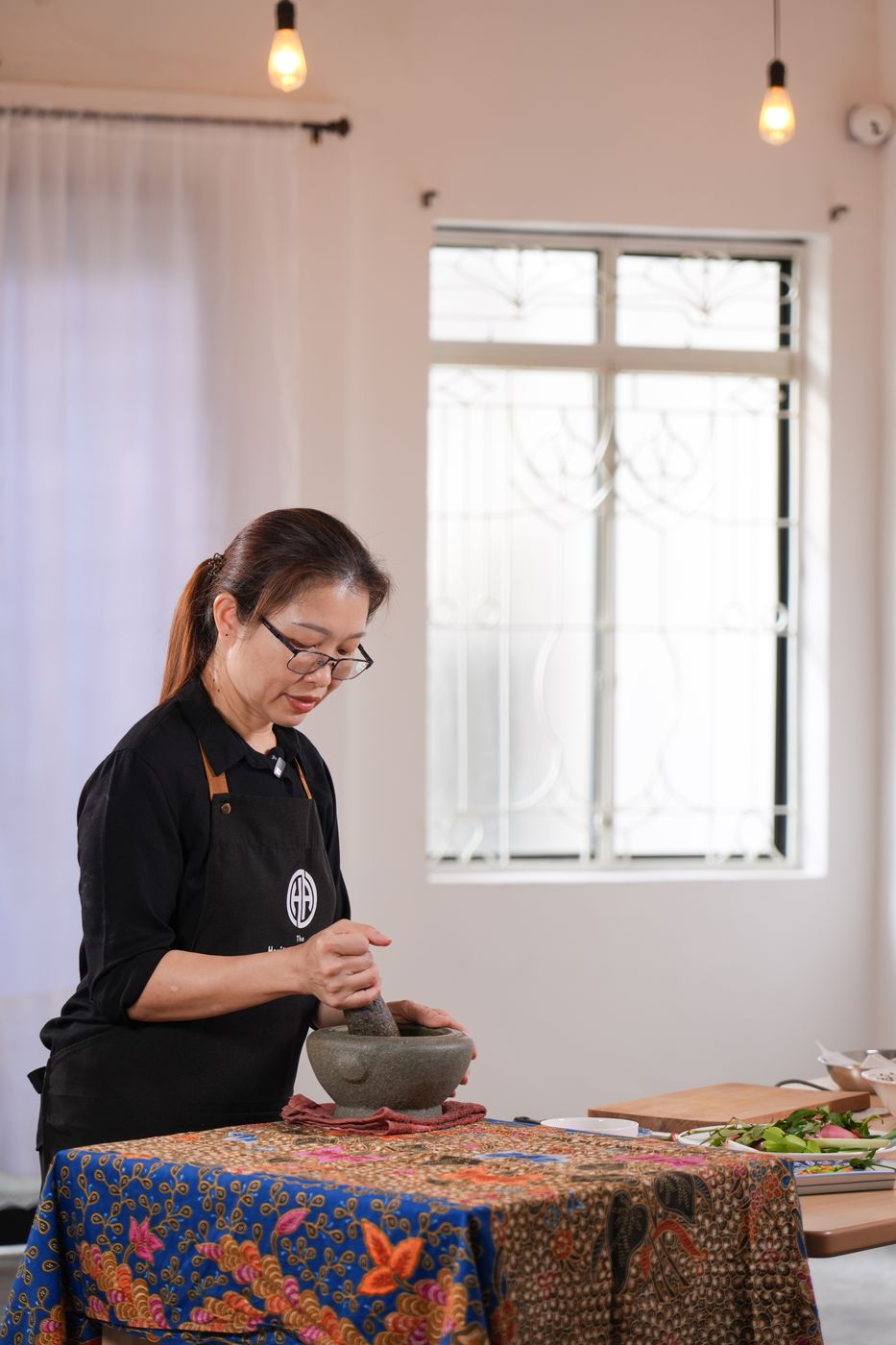 Nyonya Su Pei pounding rempah in a granite mortar